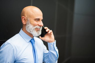 Gülümseyen bir işadamı, siyah duvarın yanında telefonla konuşuyor.