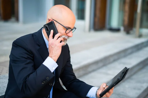 Łysy Biznesmen Białą Brodą Korzystający Tabletu Podczas Rozmowy Telefonicznej Nowoczesnym — Zdjęcie stockowe