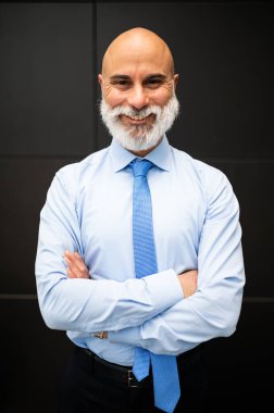 Olgun, kel, şık bir iş adamı portresi. Açık havada beyaz sakallı, kolları katlanmış.