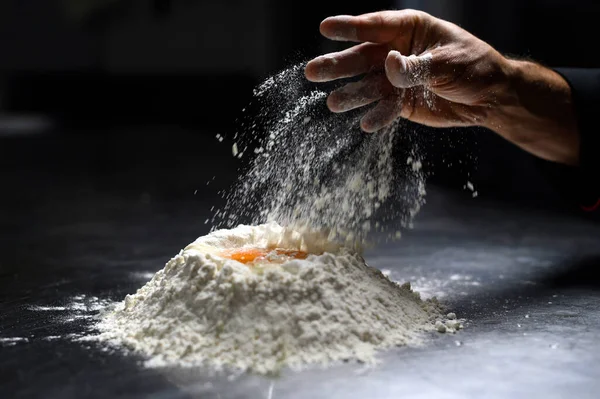 Closeup of chef\'s hand sprinkling flour, dark background
