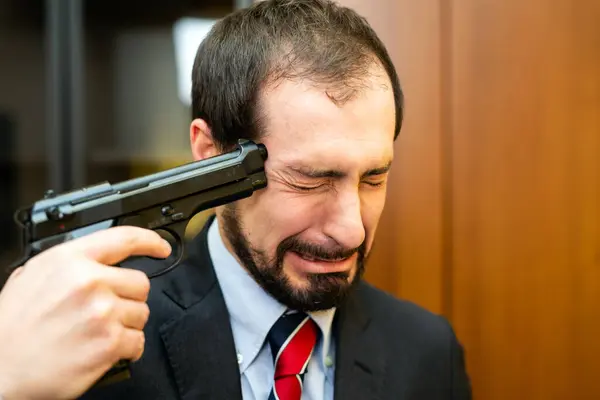 Businessman working on laptop with someone pointing a gun at his head