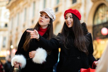 İki genç kadın gülümseyerek çekici şehirde alışveriş