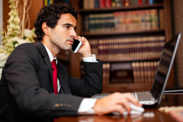 Confident male executive multitasks with a phone call and computer work in a sophisticated office setting