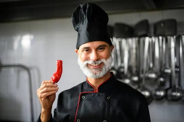 Cheerful male chef in a professional kitchen presenting a hot chili pepper