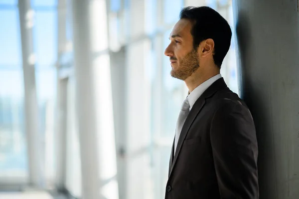 Side profile of a contemplative businessman looking out at the city in a modern office setting