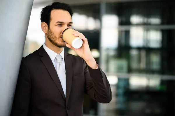 Young professional sips coffee outside an office building, taking a break from work