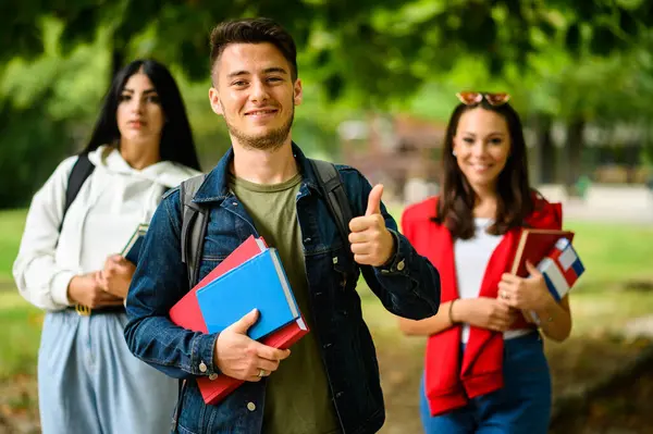 Young Male Student Gives Thumbs Female Classmates Background Outdoors — Stock Photo, Image