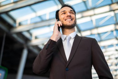 Takım elbiseli neşeli genç bir erkek dışarıda bir telefon görüşmesi yapıyor.