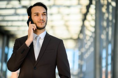 Kendine güvenen genç profesyonel bir erkek ofis binasının dışında bir telefon görüşmesi yapıyor.