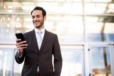 Takım elbiseli genç adam modern şehir ortamında cep telefonunun keyfini çıkarıyor.