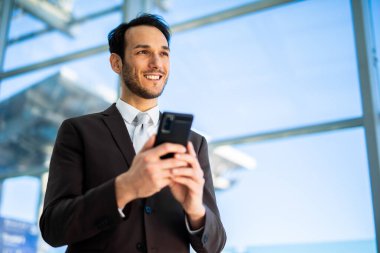 Çağdaş bir ofis ortamında telefonuyla mesajlaşan neşeli, genç bir profesyonel.