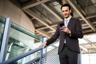 Modern bir tren istasyonunda beklerken cep telefonu kullanan genç bir profesyonel.