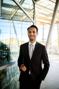 Elinde tabletle gülümseyen işadamı, günışığı altındaki çağdaş ofis lobisinde duruyor.