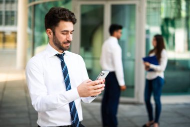 Açık havada akıllı telefon kullanan yakışıklı genç bir yönetici.