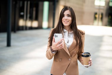 Güzel genç bayan yönetici dışarıda kahve içerken akıllı telefonunu kullanıyor.
