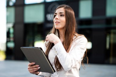 Dijital tablet kullanan genç bir iş kadını bankta oturuyor.