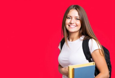 Ders kitapları ve kırmızı bir arkaplan önünde sırt çantası olan neşeli genç bir kadın, bir öğrenci olarak kendine güveni somutlaştırıyor.