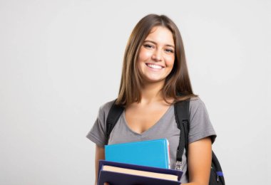 Ders kitapları ve sırt çantasıyla okula hazır, kendine güveni ve pozitifliği olan mutlu genç bir kadın.