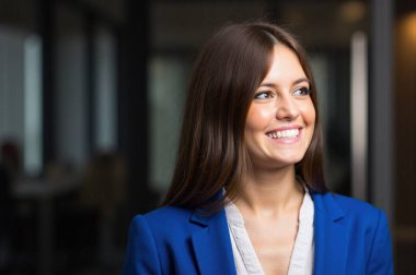 Ofiste kendine güvenen bir iş kadını, gülümseyen ve yüzünü çeviren, başarı ve iyimserlik saçan. Mutlu ve umut verici ifade, ilham verici atmosfer.