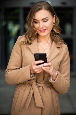 Güzel genç bayan yönetici dışarıda akıllı telefonunu kullanıyor.