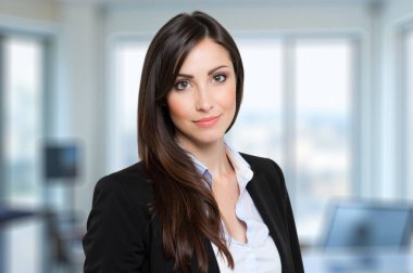 Modern ofisteki kendine güvenen genç iş kadını, başarı ve profesyonellik saçıyor. Gülümseyen, şık ve hırslı, kariyerinde gelişiyor. Şehir manzarası arkaplanı