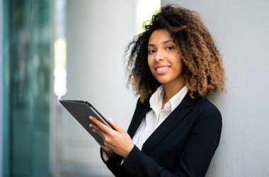 Gülümseyen Afro-Amerikan iş kadını dijital tablet kullanarak duvarda yatıyor.