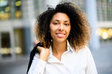 Kendine güvenen genç Afro-Amerikan bayan yönetici dışarıda modern şehir ortamında ceketini tutuyor.