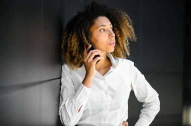 Beyaz saçlı, afro saçlı genç müdür ciddi bir telefon görüşmesi yapıyor. Ofis ortamında düşünceli ve endişeli görünüyor.