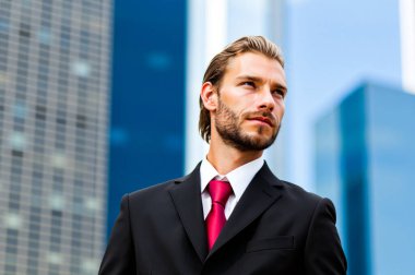 Sivri takım elbiseli kendine güvenen işadamı gökyüzüne bakıyor, hırsı ve şehir ortamındaki başarıyı somutlaştırıyor.