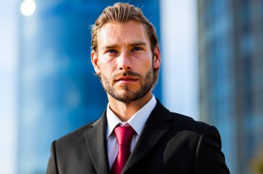 Kendine güvenen, takım elbiseli genç işadamı ofis binasının önünde poz veriyor, iş dünyasında profesyonellik ve başarı yayıyor.