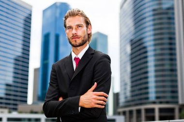 Gökdelenlerin önünde duran kendinden emin genç işadamı modern bir şehir ortamında azim ve başarı yayıyor.