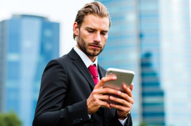 Sivri takım elbiseli kendine güvenen işadamı hareketli şehirde tablet kullanıyor, mali ve ağ bağlantılarını yönetiyor