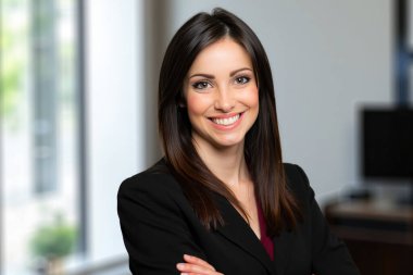 Kendine güvenen iş kadını kollarını kavuşturarak gülümsüyor, modern ofis ortamında profesyonellik ve başarı yayıyor.