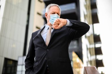 Kıdemli işadamı maske takarken saati kontrol ediyor, koronavirüs konsepti