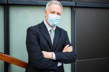 Olgun bir iş adamı maske takıyor ve kollarını kavuşturuyor.