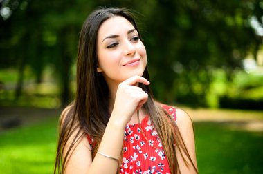 Etrafı yeşilliklerle çevrili neşeli bir yüzü olan düşünceli genç kadın.