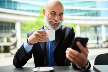 Açık havada akıllı telefon kullanarak gülümseyen olgun bir işadamı.