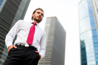 Finans bölgesinde elleri cebinde duran genç ve kendinden emin bir iş adamının portresi. Etrafındaki gökdelenlere bakıyor.