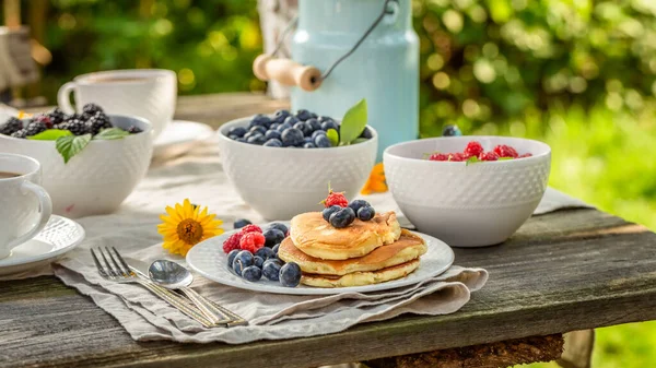 美味而自制的美式薄饼 配上蜂蜜和蓝莓 在一个阳光灿烂的早晨在花园里吃早餐 — 图库照片