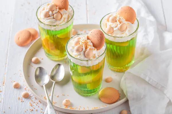 Sweet green jelly with peaches, cream and sprinkles. Green jelly with peaches and biscuits.