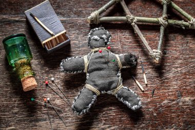 Voodoo doll, poisoned, burns and stabbed with a needle on old book as a Halloween background clipart