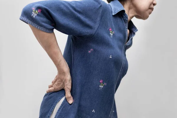 Elderly Asian woman suffering from low back pain, massaging her back to relieve pain. Geriatric society. Medical issue.