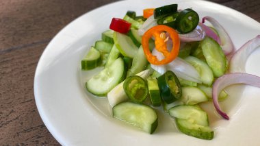 Close up of sauce for pork satay, pickles which are cucumber slices and onions in vinegar, serving on white plate  