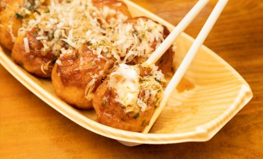 Takoyaki ya da yemek çubuğundaki ahtapot toplarını kapatın. Ahşap arka planda Japon yemekleri.