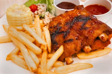 Lezzetli kızarmış domuz pirzolası, patates kızartması, mısır, domates, salata ve iki farklı sosla servis ediliyor.