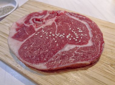 Yakın plan taze, kırmızı, çiğ pirzola bifteği güzel beyaz mermer ve susam tohumları serpiştirilmiş.