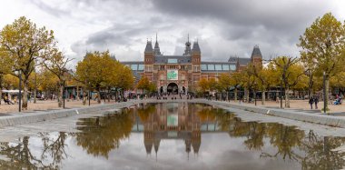 Bulutlu bir sonbahar gününde Amsterdam 'daki Rijksmuseum' un ana cephesinin bir resmi ve gölün yakınındaki yansıması..