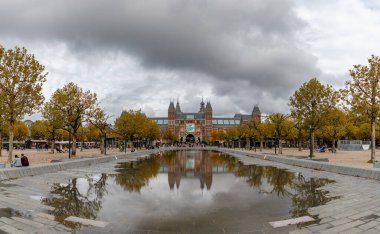 Bulutlu bir sonbahar gününde Amsterdam 'daki Rijksmuseum' un ana cephesinin bir resmi ve gölün yakınındaki yansıması..