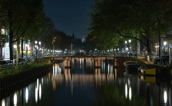 アムステルダムの夜にライトアップされた運河の橋の写真 — ストック写真