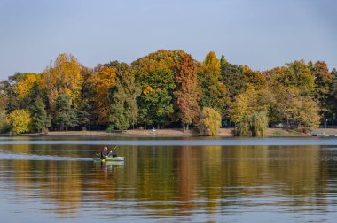 A picture of the Herastrau Lake and Park in the fall while a man kayaks in the left.